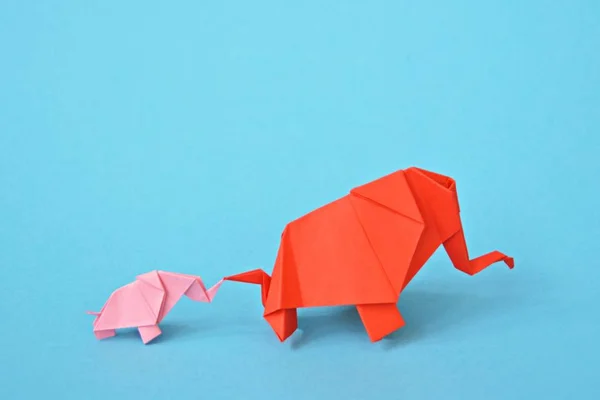 Two paper-folded elephants in pink and red stand on a blue background - concept with a little baby elephant and a mother elephant folded according to the origami technique