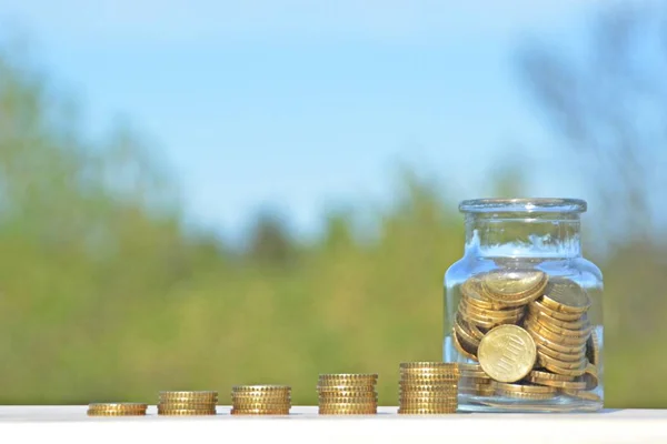 A jar full of savings stands on a space next to a purse of saved coins that pile up to form a tall tower - saving concept with room for text or other items