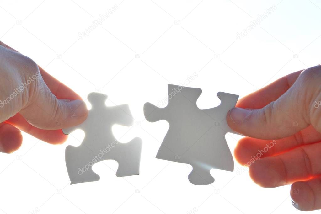 A person holds two puzzle pieces in his hand that fit together, in the background the sun shines and illuminates the parts from behind - concept for brainstorming in the professional environment