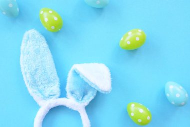Mavi tavşan kulakları ile bir kafa bandı mavi bir yüzey üzerinde yatıyor, yanında onlara beyaz nokta ile renkli Paskalya yumurtaları - bir kafa bandı ve plastik yumurta ile Paskalya için kavram