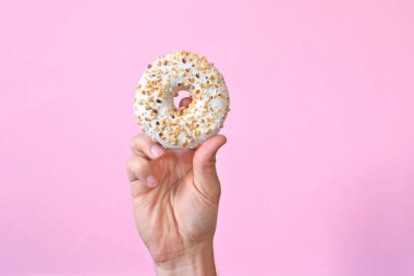 Bir el Çikolata buzlanma ile bir donut tutar yukarı. Arka plan renkli ve metin veya diğer unsurlar için oda bırakır