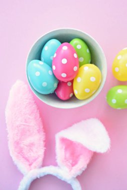 Üzerinde tavşan kulakları olan bir saç bandı pembe bir arka plan üzerinde, yanında beyaz noktalı Paskalya yumurtaları dolu bir eşarp - pastel renkleri ile Paskalya için renkler ile kavram -