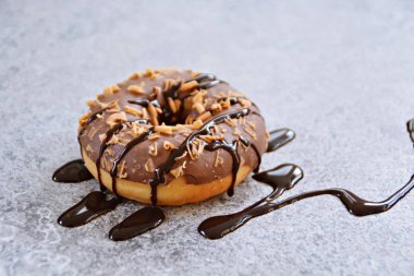 Çikolata sır ve karamel slivers ile bir donut gri mermer yüzeyinde yatıyor ve çikolata sosu ile üzerine dökülür