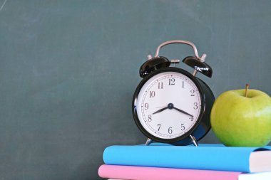 Bir çalar saat renkli kitaplar ve yeşil elma ile bir tahta önünde duruyor - ilköğretim okulunda okul ve zaman yönetimi konusunda metin veya diğer unsurlar için alan ile kavram