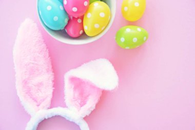 Üzerinde tavşan kulakları olan bir saç bandı pembe bir arka plan üzerinde, yanında beyaz noktalı Paskalya yumurtaları dolu bir eşarp - pastel renkleri ile Paskalya için renkler ile kavram -