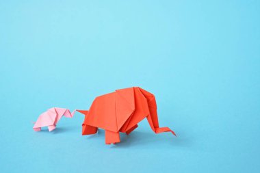 Mavi bir arka plan üzerinde pembe ve kırmızı stand iki kağıt katlanmış filler - küçük bir bebek fil ve origami tekniğine göre katlanmış bir anne fil ile kavram