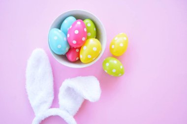 Üzerinde tavşan kulakları olan bir saç bandı pembe bir arka plan üzerinde, yanında beyaz noktalı Paskalya yumurtaları dolu bir eşarp - pastel renkleri ile Paskalya için renkler ile kavram -