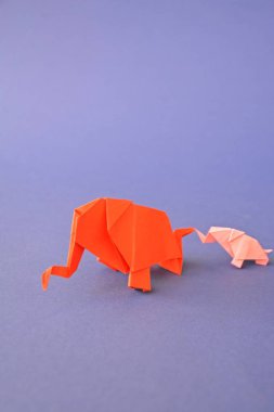 Küçük ve büyük bir origami fil iki fil gibi görünen bir ayna parçası önünde tek renkli bir yüzey üzerinde kırmızı ve pembe kağıt standı katlanmış bir su deliğinin önünde duruyor 