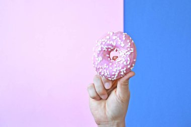 Bir el Çikolata buzlanma ile bir donut tutar yukarı. Arka plan renkli ve metin veya diğer unsurlar için oda bırakır