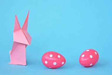 Pastel kağıt tan katlanmış pembe bir origami tavşan ı da beyaz nokta ile Paskalya yumurtası olan mavi bir taban üzerinde duruyor - origami ve metin veya Paskalya için diğer unsurlar için alan kavramı 