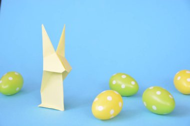 Pastel kağıt tan katlanmış pembe bir origami tavşan ı da beyaz nokta ile Paskalya yumurtası olan mavi bir taban üzerinde duruyor - origami ve metin veya Paskalya için diğer unsurlar için alan kavramı 