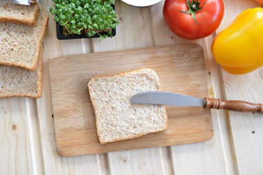 Kaba-taneli krem peyniri ve Cress ile bir kepekli tost bir bıçak yanında bir tahta tahta ve biber ve domates gibi sebze, yanı sıra Cress, salatalık ve havuç bir masada yatıyor