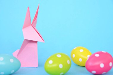Pastel kağıt tan katlanmış pembe bir origami tavşan ı da beyaz nokta ile Paskalya yumurtası olan mavi bir taban üzerinde duruyor - origami ve metin veya Paskalya için diğer unsurlar için alan kavramı 