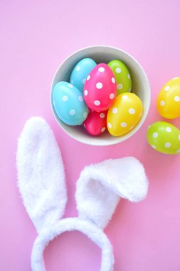 Üzerinde tavşan kulakları olan bir saç bandı pembe bir arka plan üzerinde, yanında beyaz noktalı Paskalya yumurtaları dolu bir eşarp - pastel renkleri ile Paskalya için renkler ile kavram -