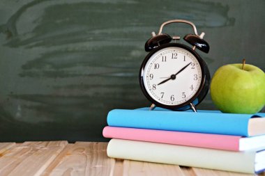 Bir çalar saat renkli kitaplar ve yeşil elma ile bir tahta önünde duruyor - ilköğretim okulunda okul ve zaman yönetimi konusunda metin veya diğer unsurlar için alan ile kavram