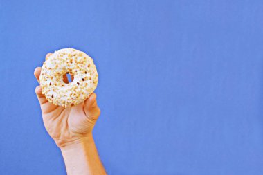 Bir el Çikolata buzlanma ile bir donut tutar yukarı. Arka plan renkli ve metin veya diğer unsurlar için oda bırakır