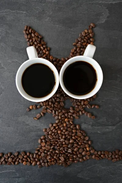 An Easter bunny made of freshly roasted coffee beans laid out with a cup of coffee - concept for fresh coffee enjoyment on easter and as easter gift in the form of coffee beans