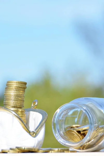 A jar full of savings stands on a space next to a purse of saved coins that pile up to form a tall tower - saving concept with room for text or other items