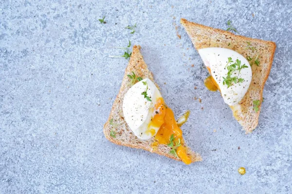 On a freshly roasted whole wheat toast is a boiled egg with soft egg yolk, which flows out of the egg. On the egg is cress and salt and pepper