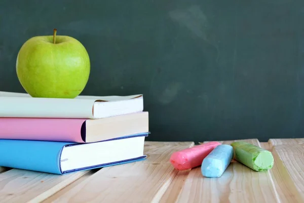 異なる色のカバーを持つ3冊の本は リンゴと黒板の前に木製の表面に横たわっている テキストや他の要素のための場所を持つ教育や学校のための概念 — ストック写真