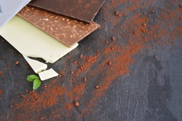 Три плитки темного шоколада, орехи и белый шоколад лежат на темной мраморной поверхности - шоколад на темной поверхности с местом для текста или других элементов
