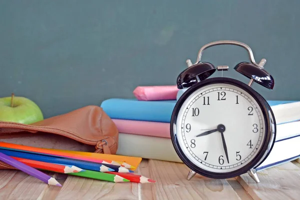 An alarm clock stands in front of a blackboard with colorful books and a green apple - concept with space for text or other elements on the subject of school and time management in elementary school