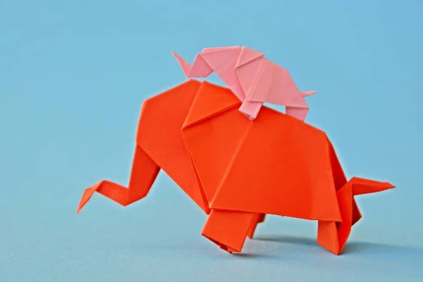 赤とピンクの紙で折りたたまれた小さな折り紙の象は 2頭の象が水の穴の前に立っているように見える鏡の破片の前にモノクロの表面に立っています — ストック写真