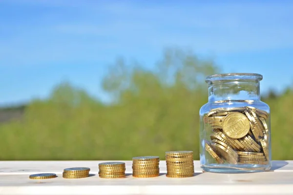 A jar full of savings stands on a space next to a purse of saved coins that pile up to form a tall tower - saving concept with room for text or other items