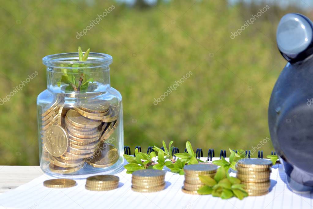 A jar full of savings stands on a space next to a purse of saved coins that pile up to form a tall tower - saving concept with room for text or other items