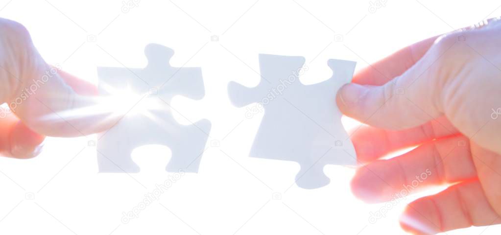 A person holds two puzzle pieces in his hand that fit together, in the background the sun shines and illuminates the parts from behind - concept for brainstorming in the professional environment