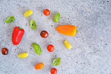 Taze sebze ile arka plan - Küçük domates baharatile kaplı gri mermer yüzeyüzerinde küçük biber ve fesleğen yaprakları ile birlikte yalan 