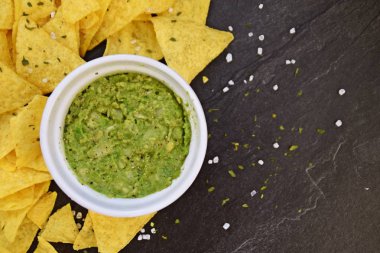 Koyu mermer bir yüzeyde soğan ve birçok baharat ile ev yapımı guacamole bir kase yanında tuz ile nachos bir yığın var - metin için alan ile lezzetli atıştırmalık