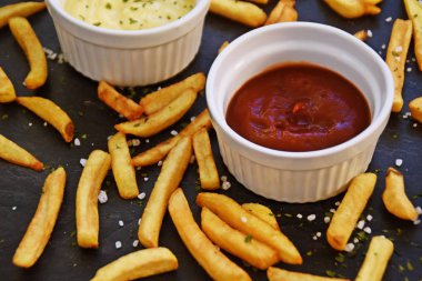 taze patates kızartması ve tuz taneleri ve baharatlar yalan koyu mermer arka plan, ketçap dolu bir kapta kızartılmış altın sarısı taze patates kızartması 