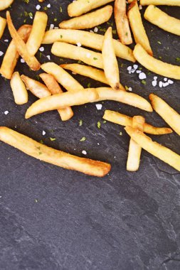 Deniz tuzu taneleri ve patates kızartması baharat ile koyu mermer yüzeyüzerinde taze patates gevrek kavrulmuş cips - Lezzetli fast food kızarmış altın sarısı