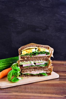 Sağlıklı bir diyet olarak peynir, sosis, yumurta ve salata ile ayçiçeği tohumu ekmek çeşitli sandviç koyu bir arka plan üzerinde yığılmış 