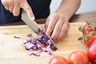 Bir kişi taze gevrek sağlıklı salata için ahşap bir tahta üzerinde kırmızı soğan keser - kişinin elinde yakın çekim - taze organik sebze ile sağlıklı beslenme için kavram