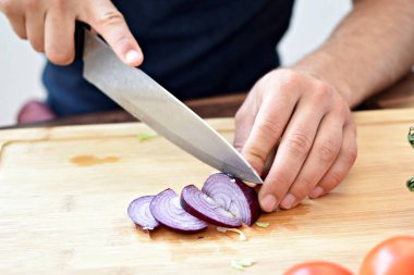 Bir kişi taze gevrek sağlıklı salata için ahşap bir tahta üzerinde kırmızı soğan keser - kişinin elinde yakın çekim - taze organik sebze ile sağlıklı beslenme için kavram