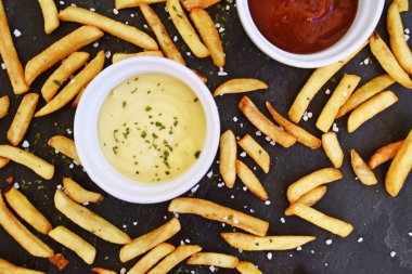  taze patates kızartması ve tuz taneleri ve baharatlar yalan koyu mermer arka plan, ketçap dolu bir kapta kızartılmış altın sarısı taze patates kızartması