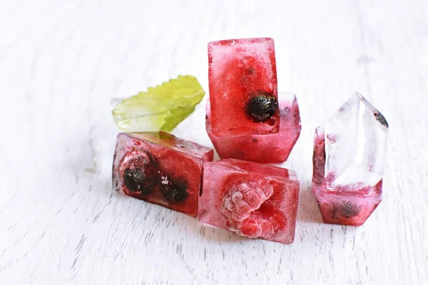 Yaz aylarında serinletici soğutma olarak, hafif ahşap bir yüzey üzerinde yalan içinde donan çeşitli çilek ile buz küpleri - Buz küpleri lezzetli ve organik çilek