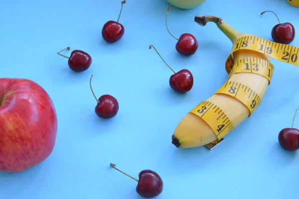 Different types of fruit, such as apples, cherries and bananas lie on a single-footed base and are wrapped in a measuring tape - concept for healthy weight loss that makes fun