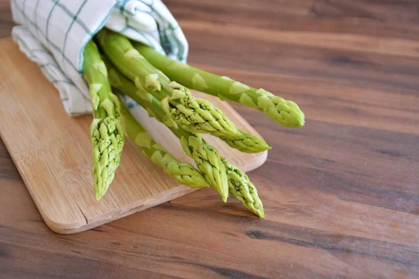 Many bars of green asparagus are uncooked on a dark marble surface