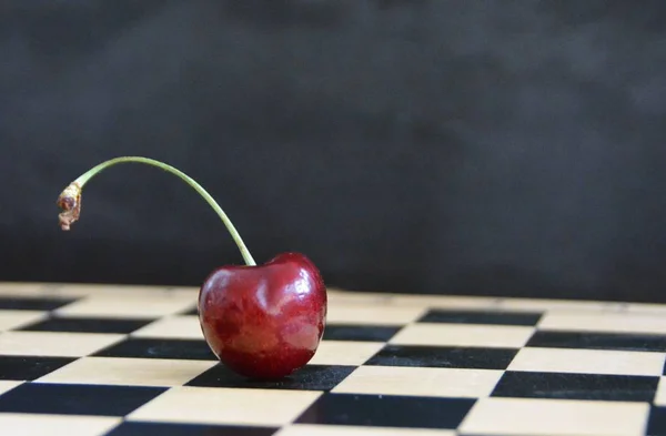 A single cherry lies on a gray marble surface