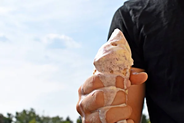 Closeup on the upper body of a man with shirt holding a waffle ice cream in hand. The ice cream balls Wildberry are already melting due to the heat - Too hot summer with refreshing cooling