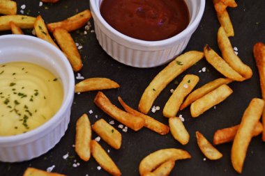  taze patates kızartması ve tuz taneleri ve baharatlar yalan koyu mermer arka plan, ketçap dolu bir kapta kızartılmış altın sarısı taze patates kızartması