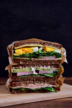 Sağlıklı bir diyet olarak peynir, sosis, yumurta ve salata ile ayçiçeği tohumu ekmek çeşitli sandviç koyu bir arka plan üzerinde yığılmış 