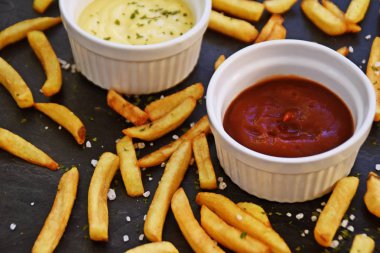 taze patates kızartması ve tuz taneleri ve baharatlar yalan koyu mermer arka plan, ketçap dolu bir kapta kızartılmış altın sarısı taze patates kızartması 