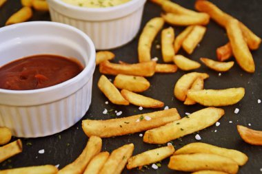 taze patates kızartması ve tuz taneleri ve baharatlar yalan koyu mermer arka plan, ketçap dolu bir kapta kızartılmış altın sarısı taze patates kızartması 