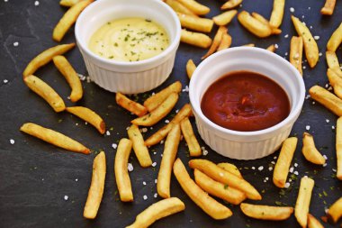 taze patates kızartması ve tuz taneleri ve baharatlar yalan koyu mermer arka plan, ketçap dolu bir kapta kızartılmış altın sarısı taze patates kızartması 