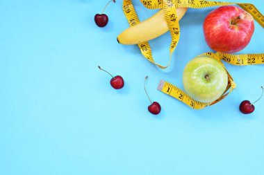 Elma, kiraz ve muz gibi farklı meyve türleri tek ayaklı bir taban üzerinde yatmaktadır ve bir ölçüm bandına sarılır - eğlenceli kılan sağlıklı kilo kaybı için kavram