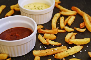 taze patates kızartması ve tuz taneleri ve baharatlar yalan koyu mermer arka plan, ketçap dolu bir kapta kızartılmış altın sarısı taze patates kızartması 